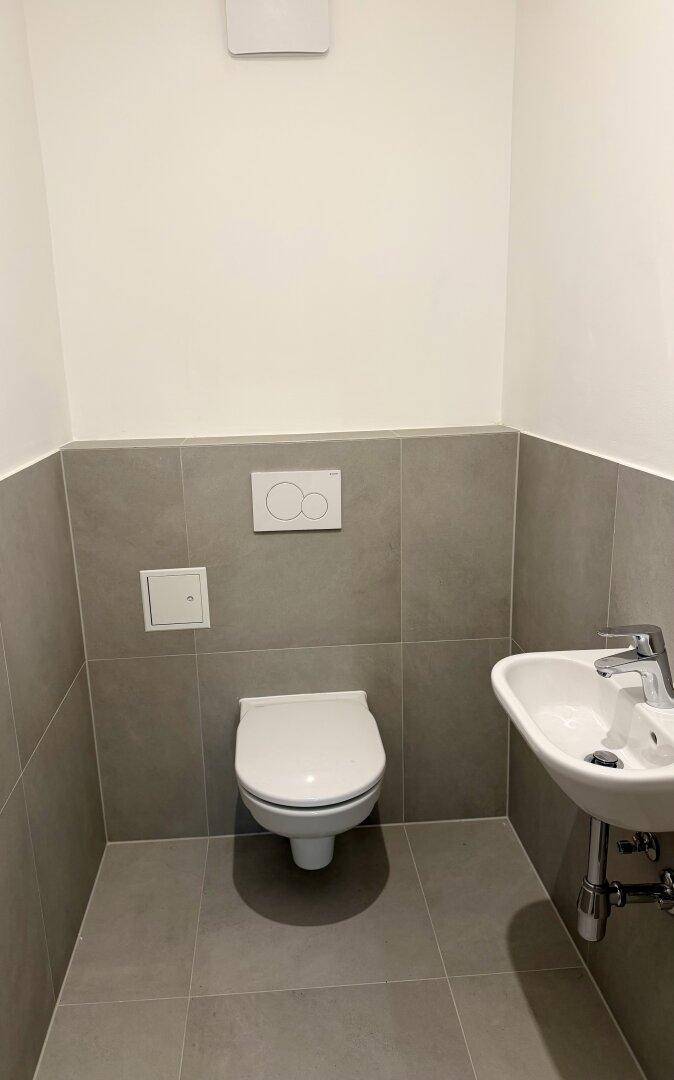 Modernes Gäste-WC mit wandhängender Toilette und kleinem Waschbecken.