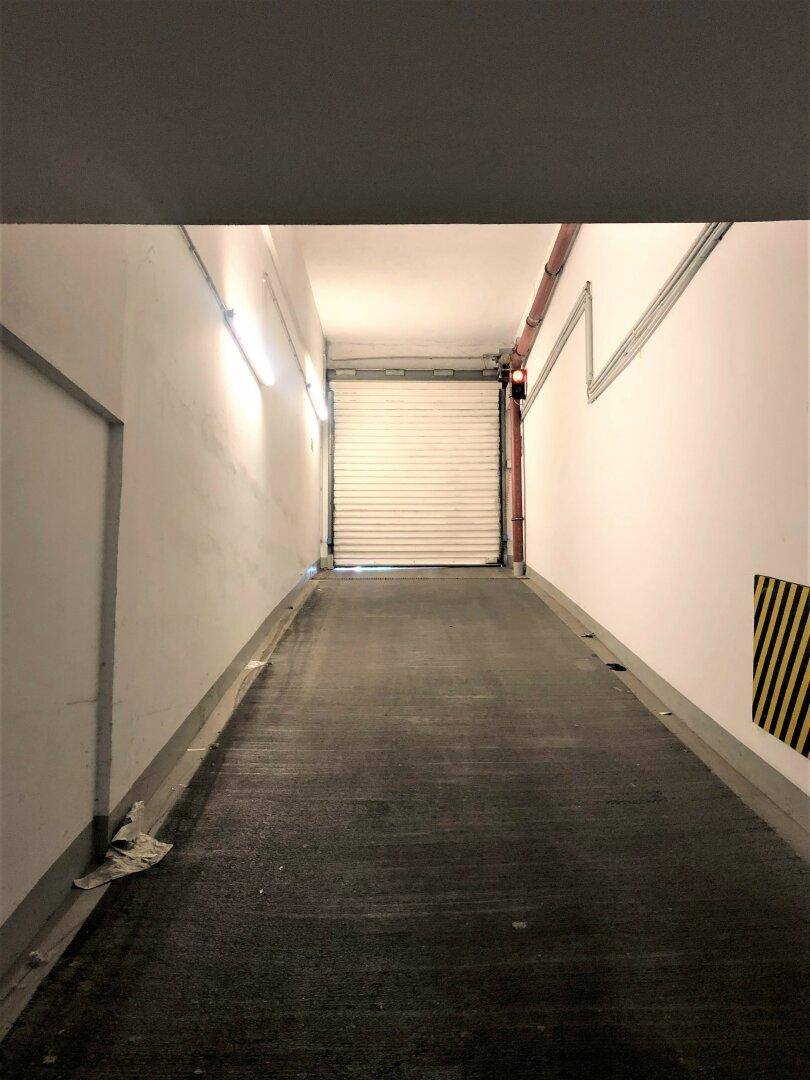 Lange Zufahrtsrampe zur Tiefgarage mit geschlossener Rolltor und Beleuchtung an den Wänden.