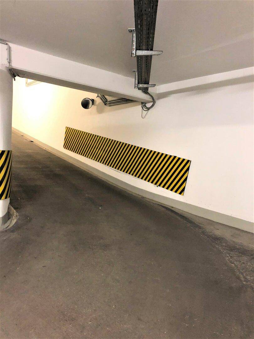 Einfahrt zur Tiefgarage mit Sicherheitskamera, Kabeltrassen und Warnstreifen an den Wänden.