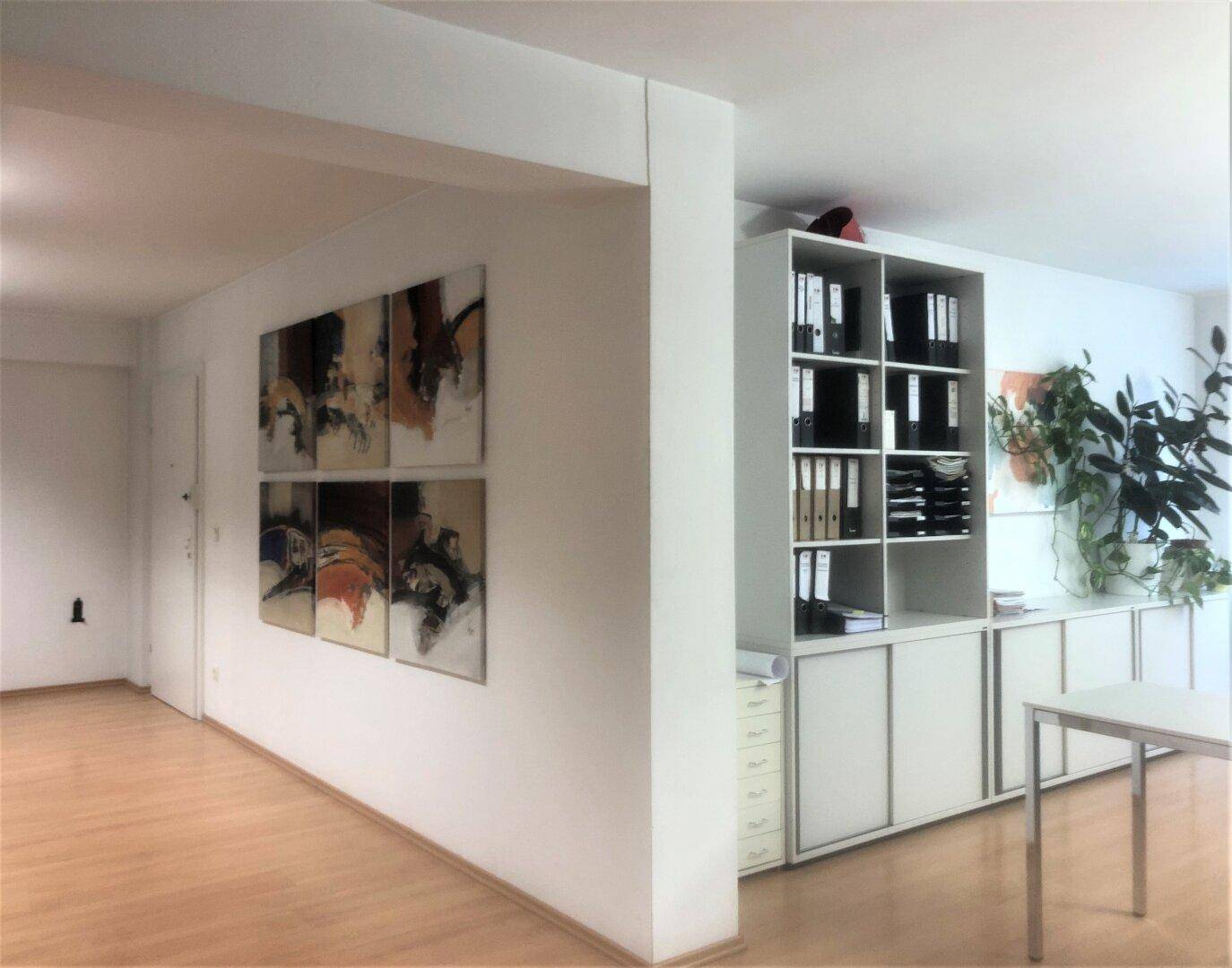 Geräumiger Bürobereich mit Holzfußboden, Kunstwerken an der Wand und integrierten Regalen für Aktenordner.