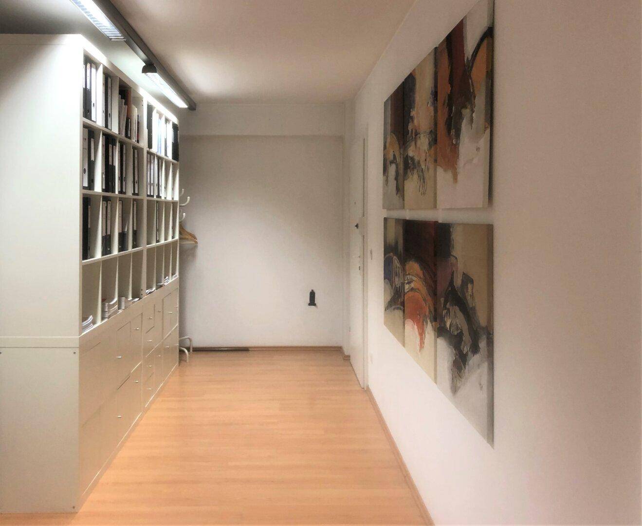 Langer Flur mit Holzfußboden, integrierten Schränken und dekorativen Wandbildern, gut beleuchtet.