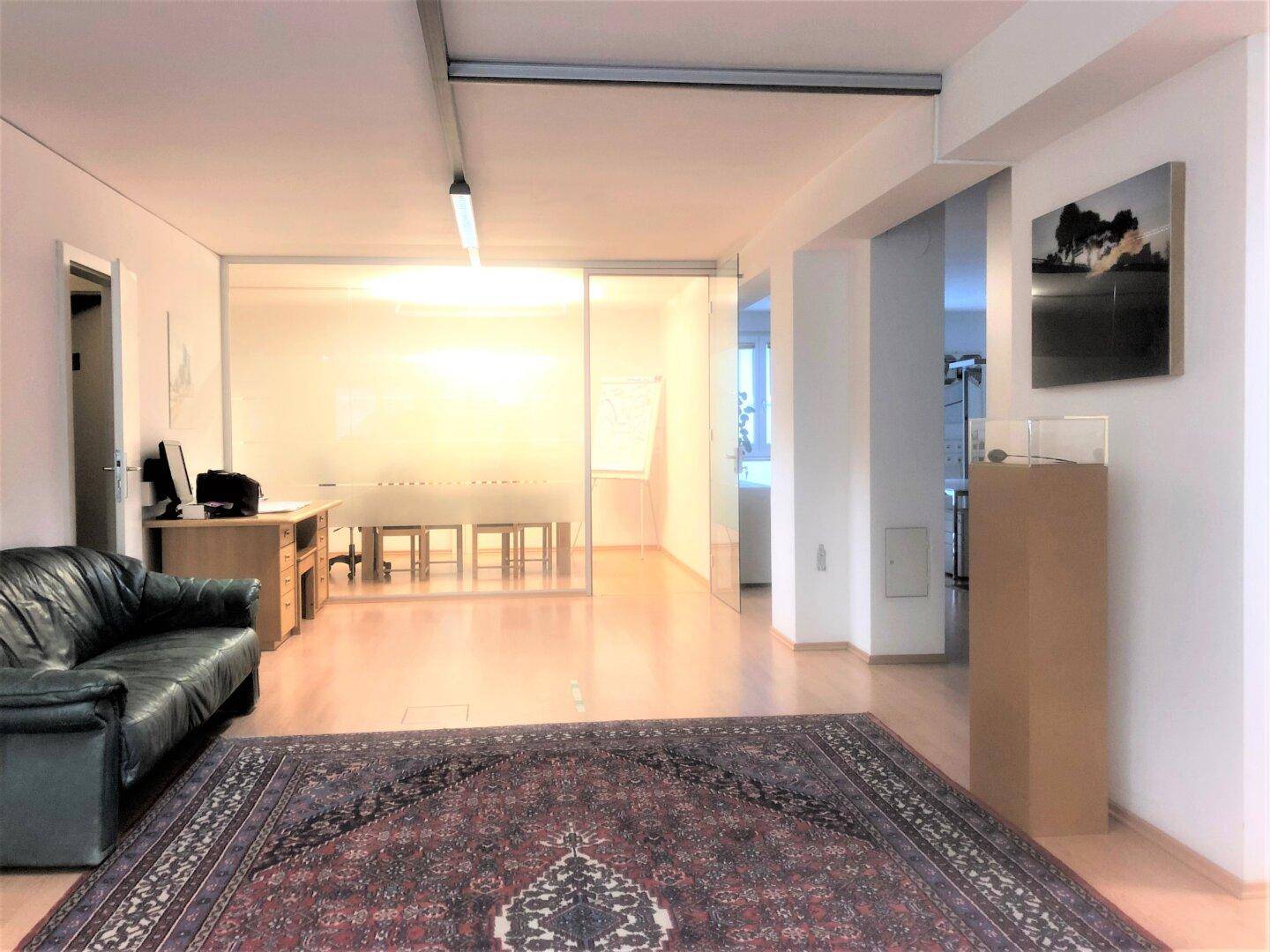 Geräumiges Büro mit Ledersofa, Schreibtisch und einem Konferenzraum hinter Glaswänden, modern gestaltet.