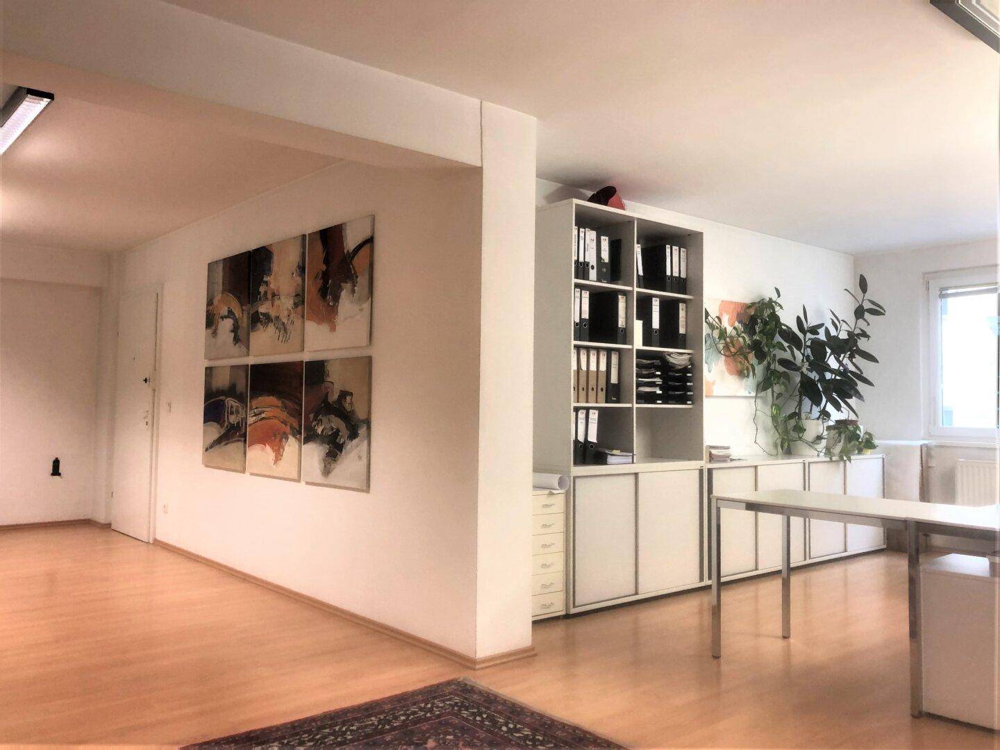 Offener Bürobereich mit Holzfußboden, Kunst an der Wand und praktischen Aufbewahrungsmöbeln, gut organisiert.