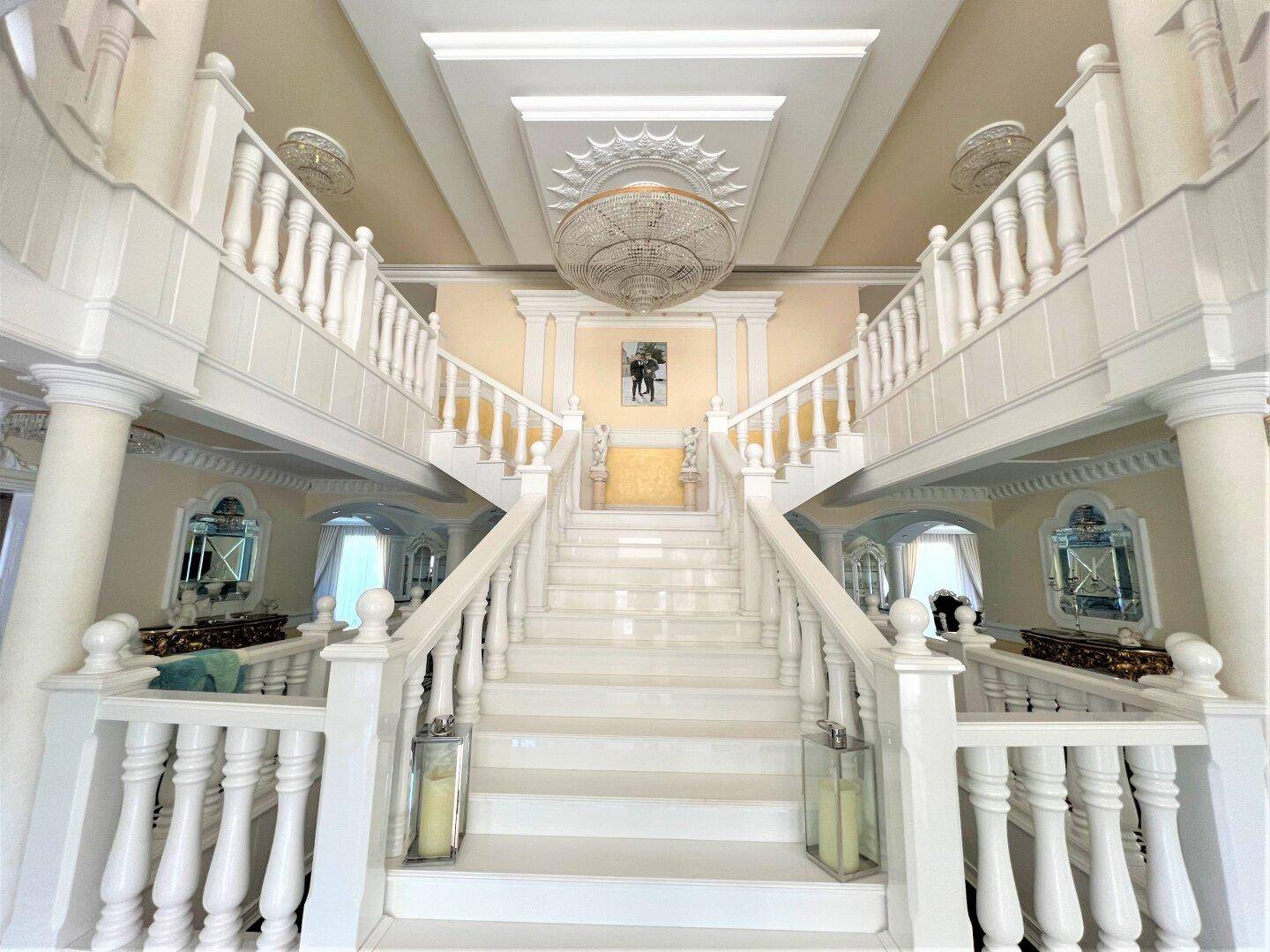Beeindruckende Marmortreppe in einer lichtdurchfluteten Eingangshalle mit eleganten Verzierungen und Kronleuchter.