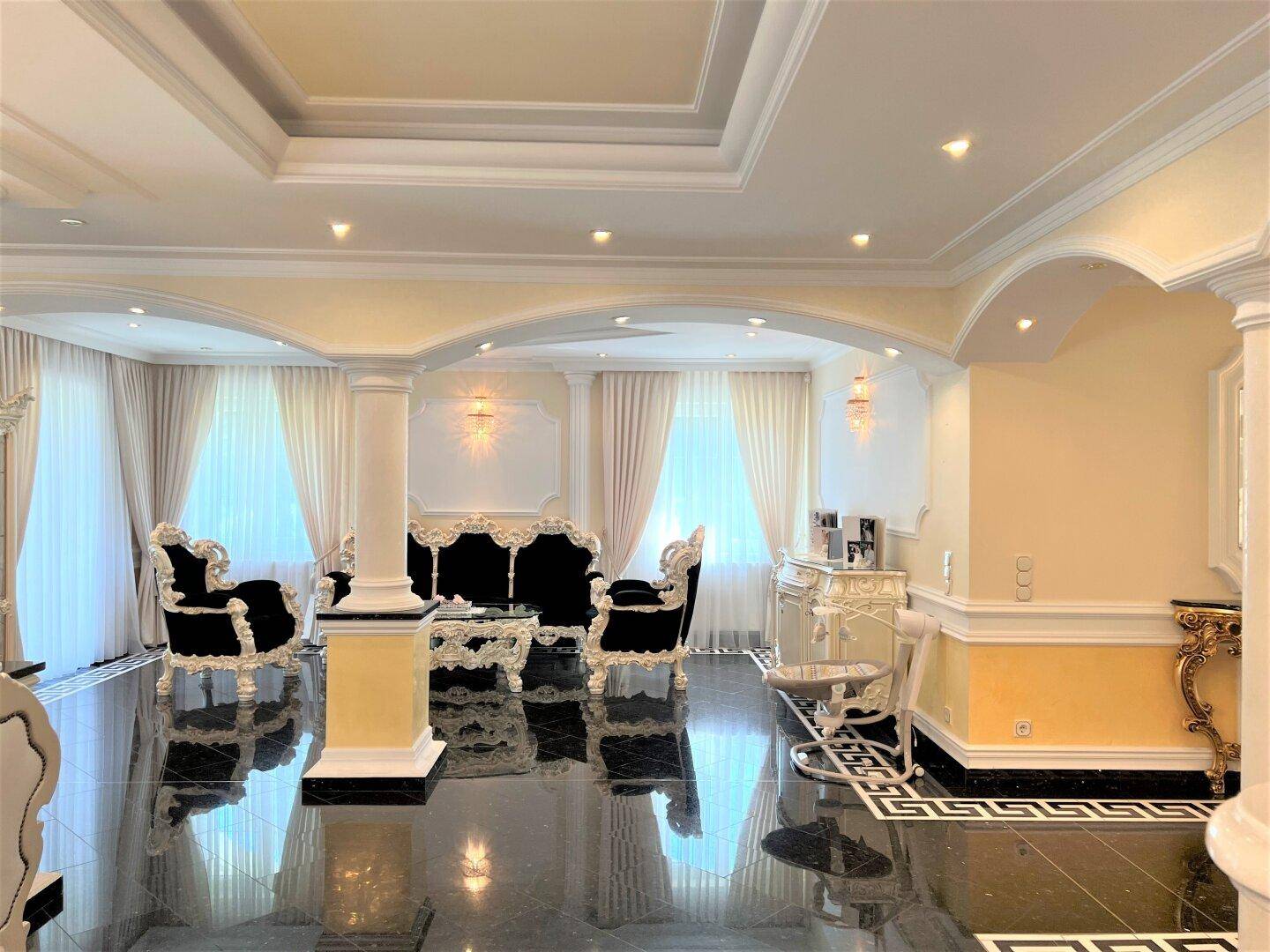 Eleganter Wohnbereich mit luxuriösen Sitzmöbeln, hohen Decken und großen Fenstern mit Vorhängen.