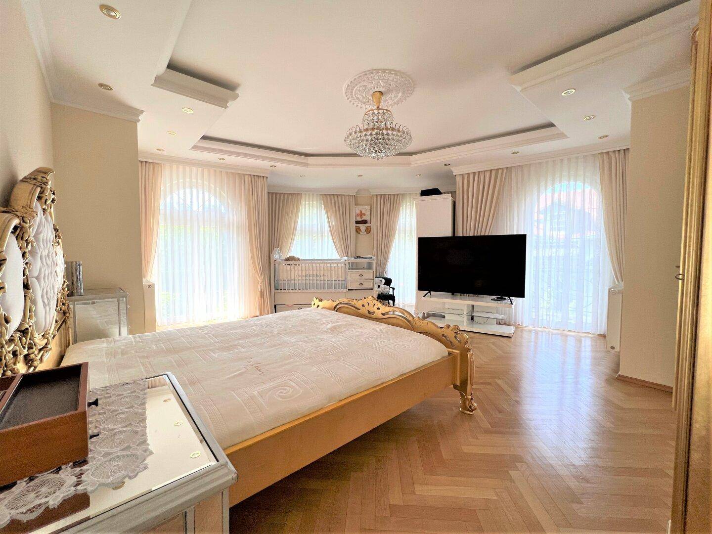 Geräumiges Schlafzimmer mit Doppelbett, Parkettboden und großen Fenstern für viel Tageslicht.