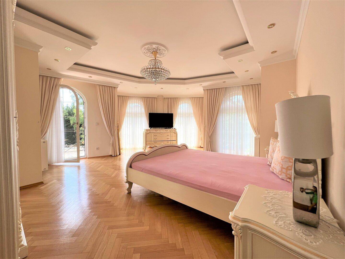 Helles Schlafzimmer mit Parkettboden, hohen Decken und Zugang zum Garten.