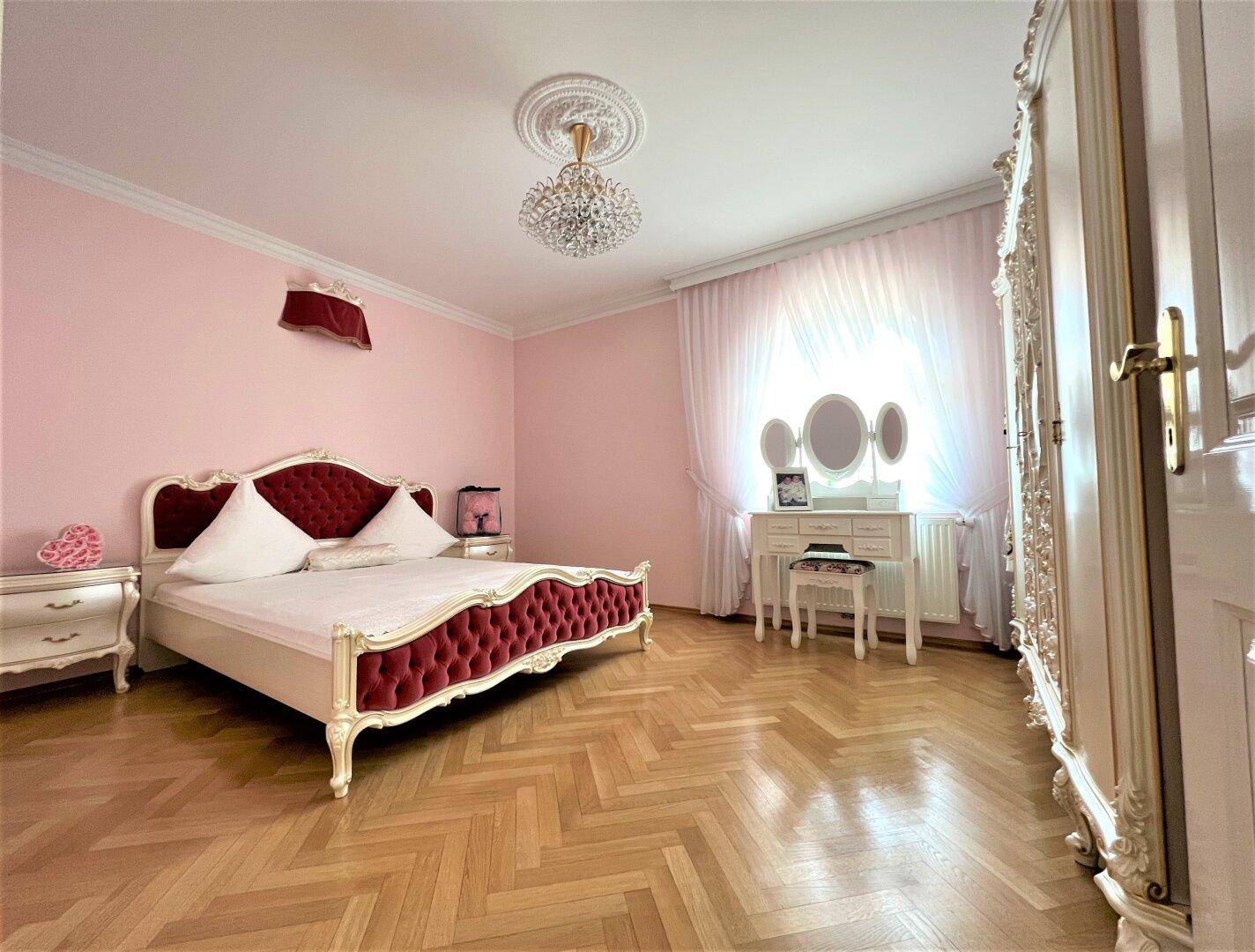 Rosa Schlafzimmer mit Parkettboden, Kronleuchter und Schminktisch.