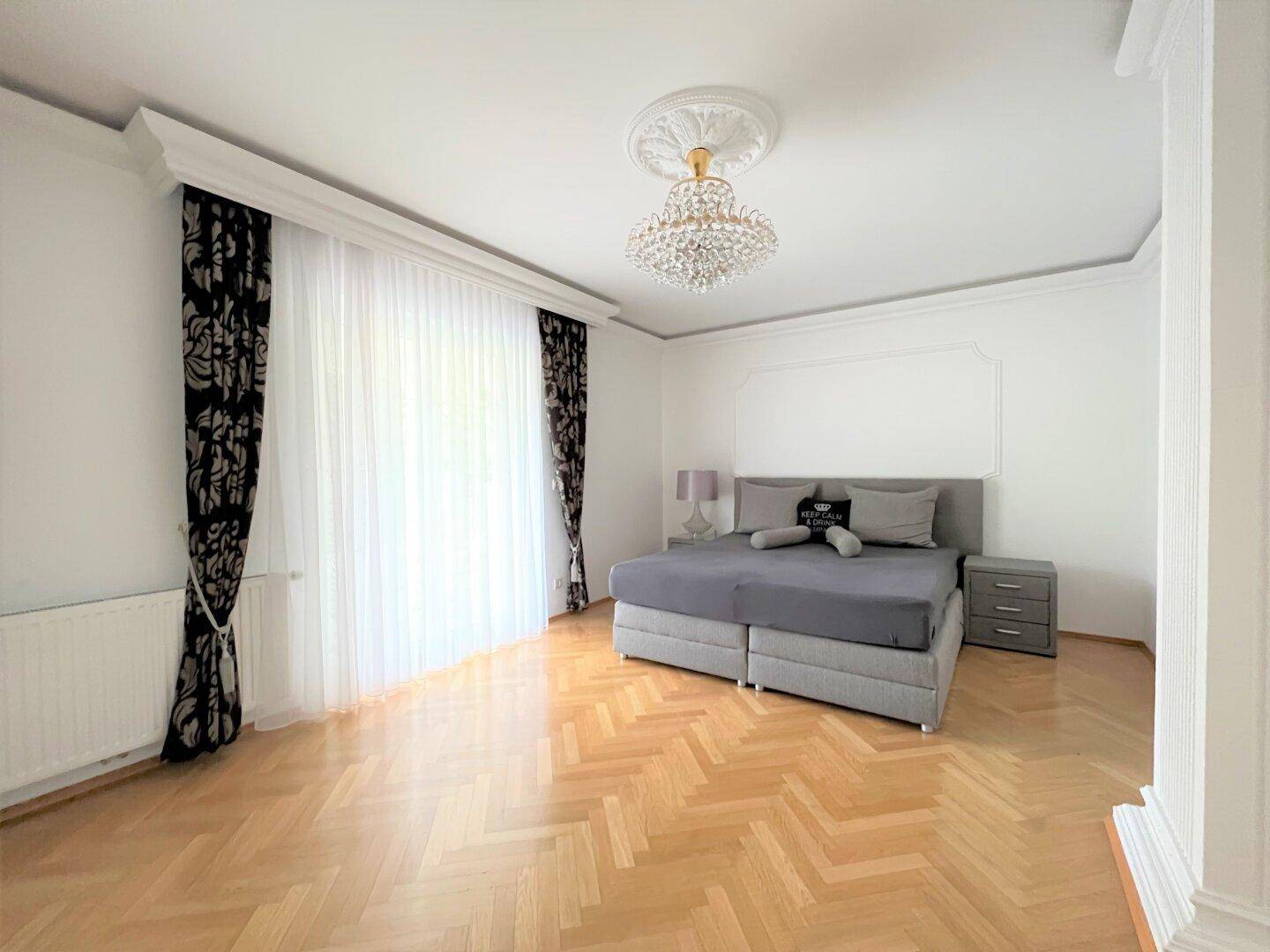 Modernes Schlafzimmer mit Parkettboden, grauen Möbeln und Kronleuchter.