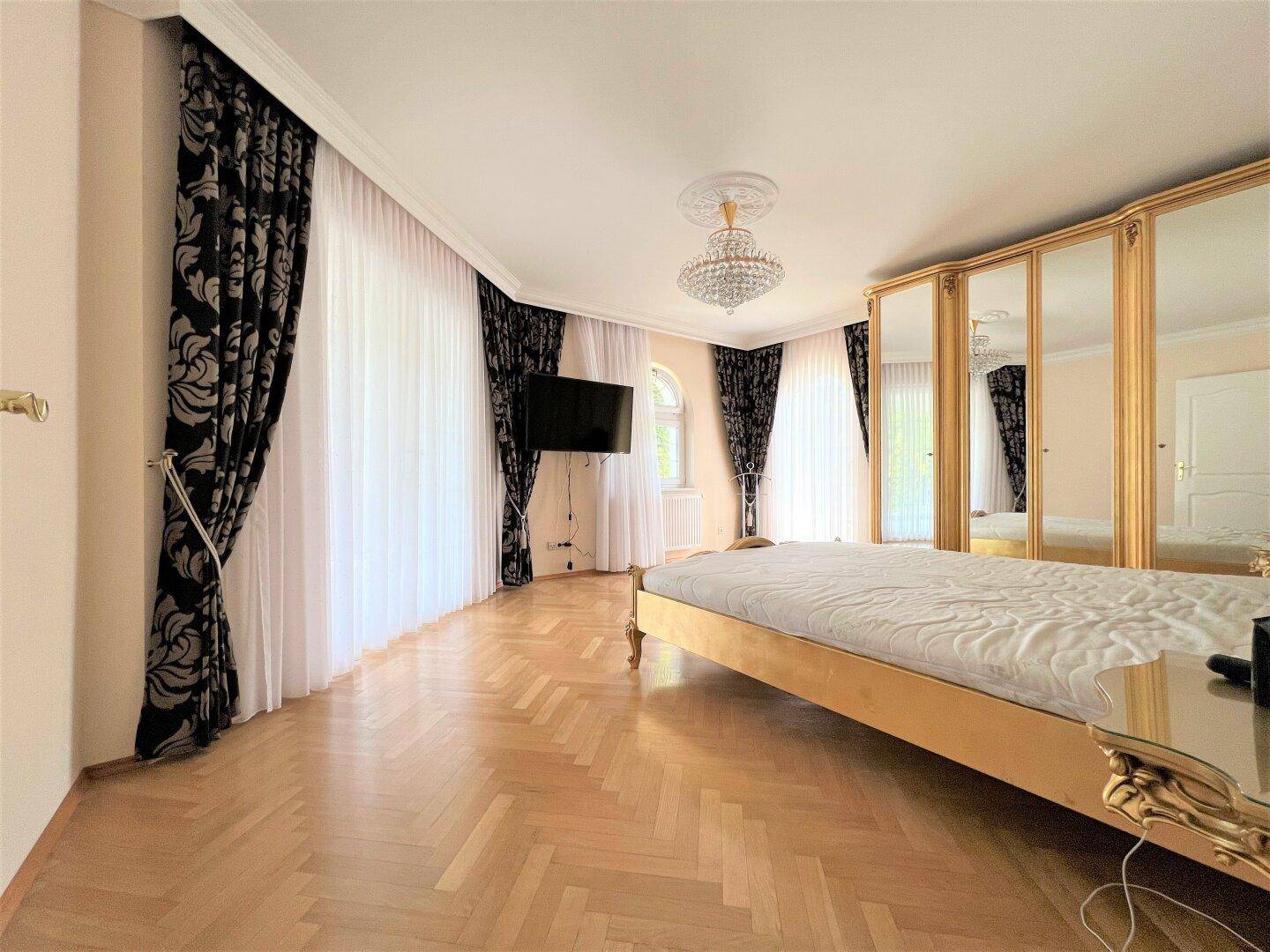 Geräumiges Schlafzimmer mit Parkettboden, Spiegelschrank und Kronleuchter.