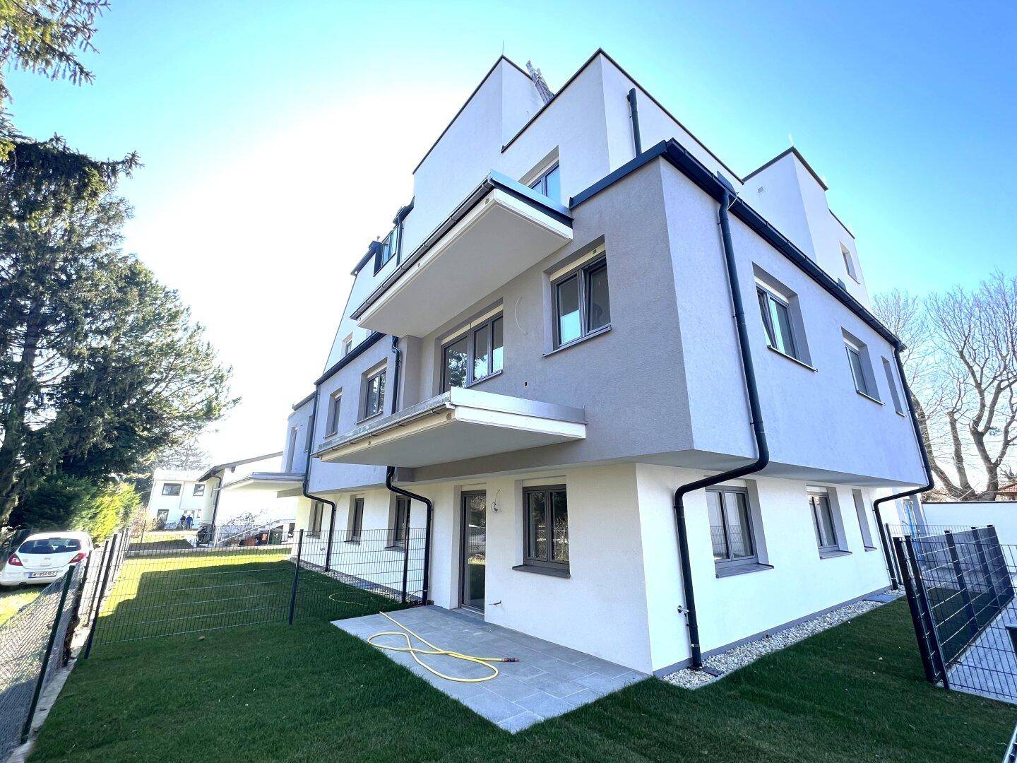 Moderne Neubaufassade mit Balkonen und gepflegtem Rasenbereich unter strahlendem Sonnenschein.