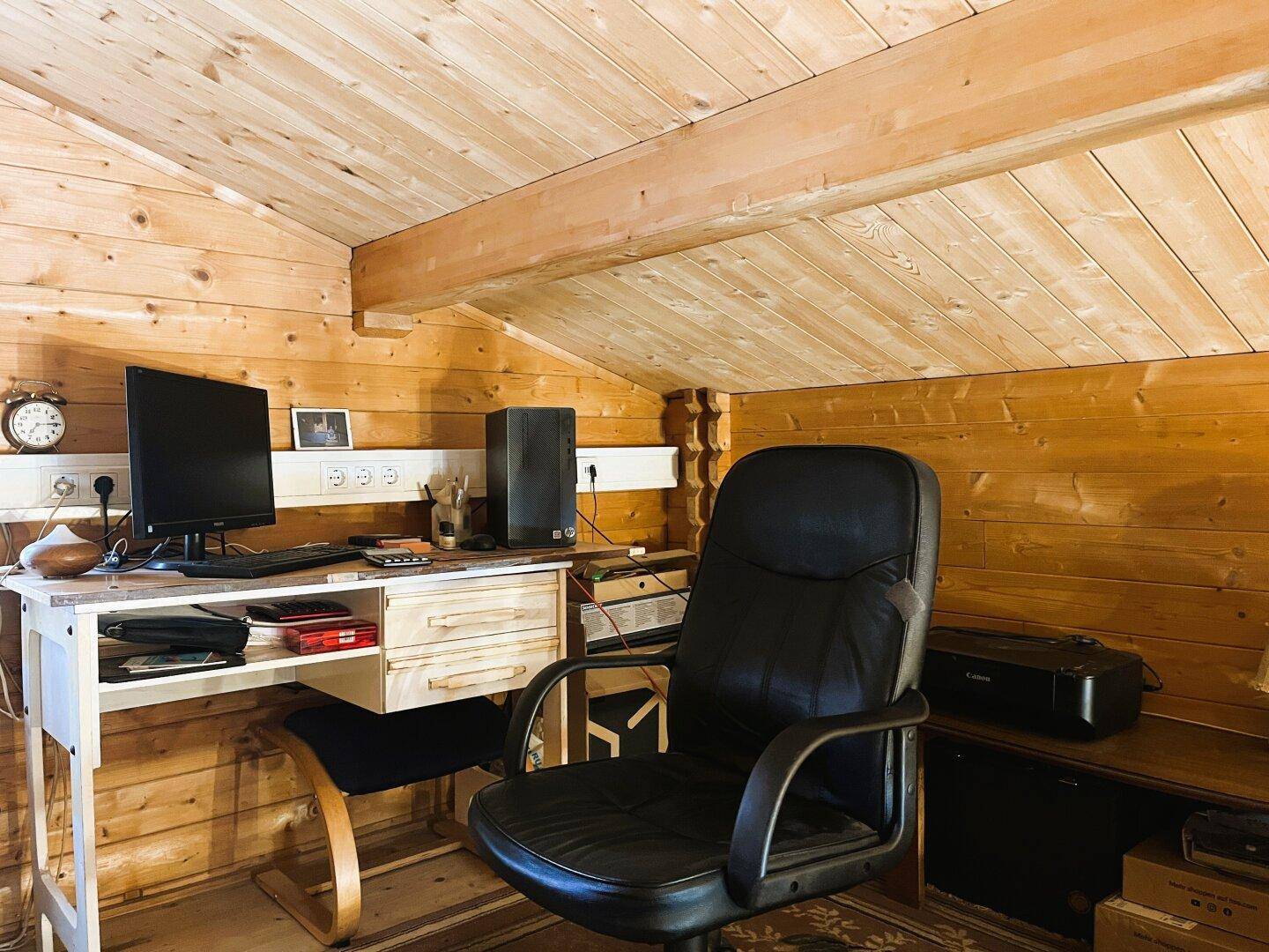 Arbeitsbereich im Dachgeschoss mit Holzwänden, Schreibtisch und Blick auf den Wohnbereich.