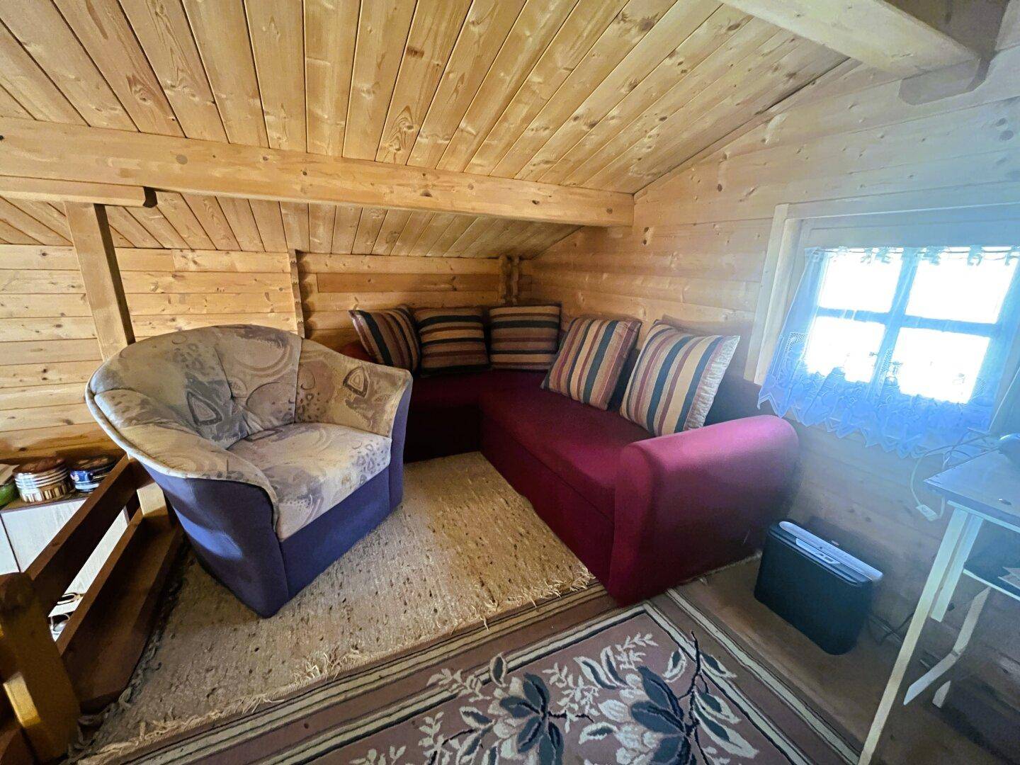 Gemütliche Sitzecke im Dachgeschoss mit Sofa, Sessel und Holzwänden.