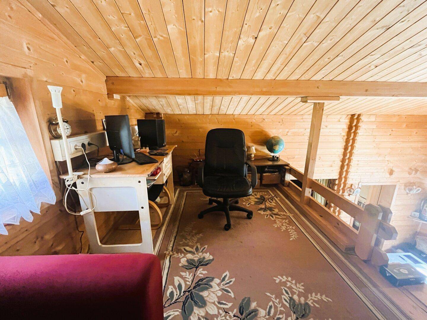 Offener Arbeitsbereich im Dachgeschoss mit Teppichboden und Blick auf das darunterliegende Wohnzimmer.