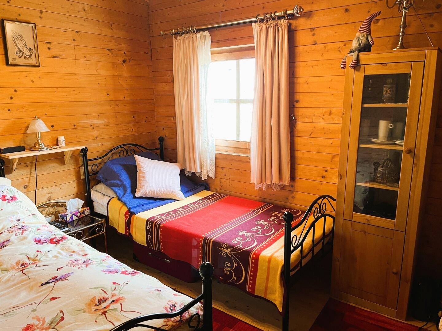 Schlafzimmer im Holzhaus mit zwei Einzelbetten, Holzwänden und einem Fenster.