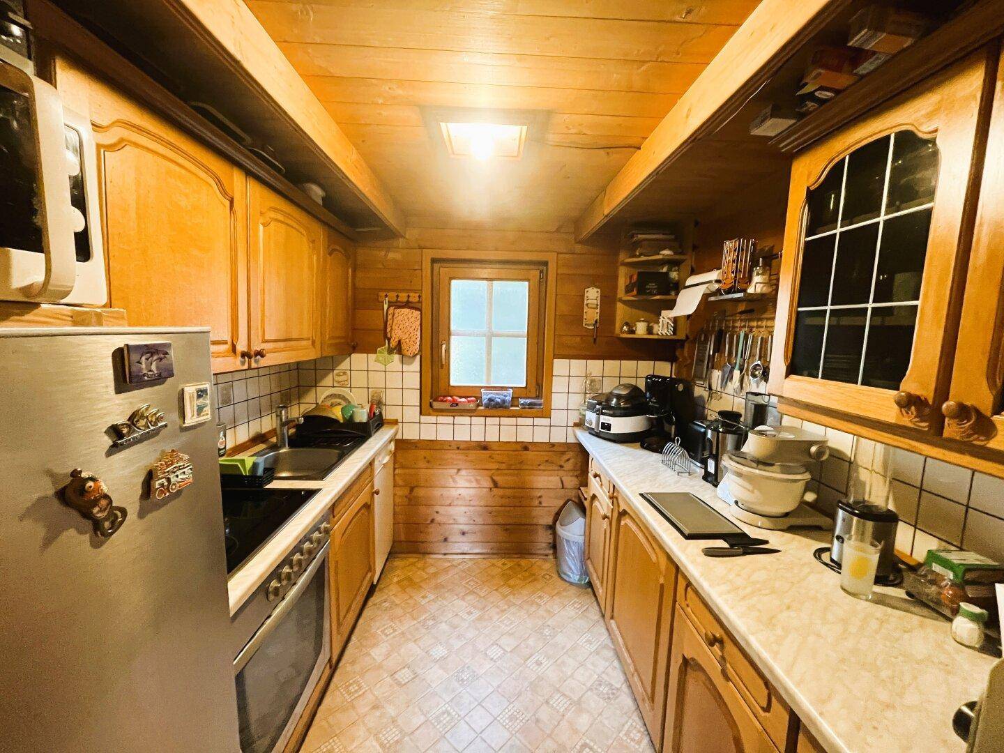 Funktionale Küche im Holzhaus mit Holzschränken, Fliesenrückwand und Fenster.