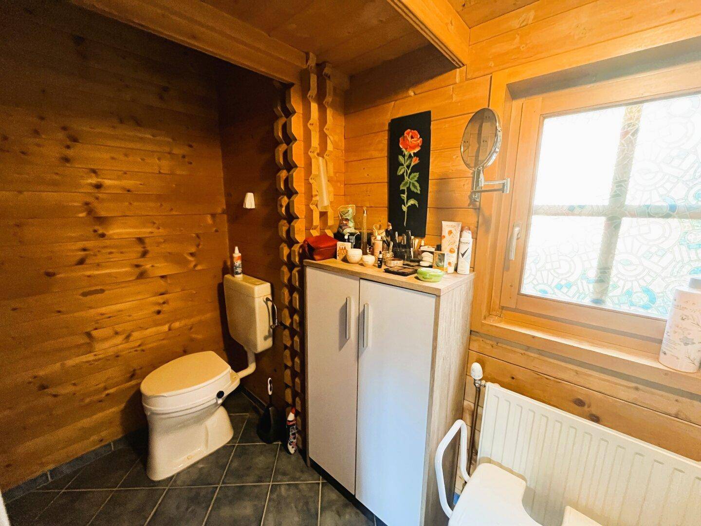 Badezimmer mit WC, Holzwänden, Fenster und einem kleinen Schrank.
