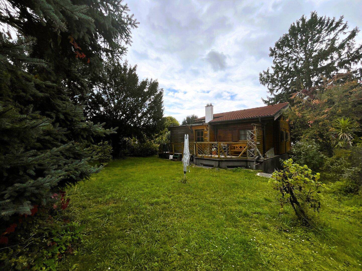 Weitläufiger Garten mit Rasenfläche und dem Holzhaus im Hintergrund, umgeben von Bäumen.
