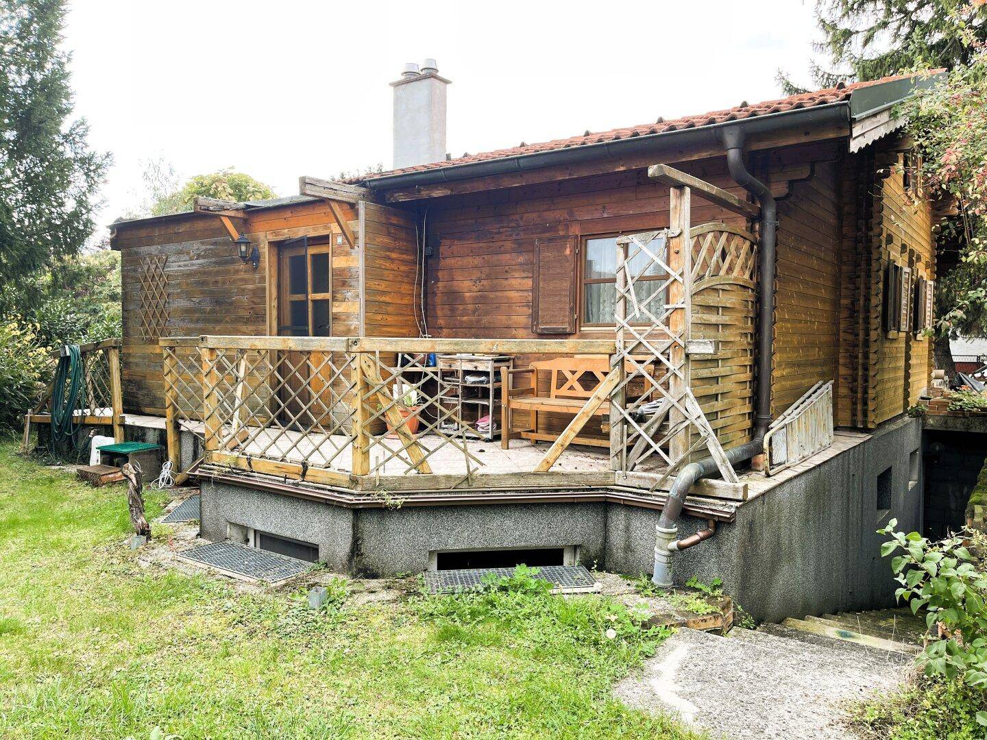 Rückseite des Holzhauses mit einer erhöhten Holzterrasse und Blick ins Grüne.
