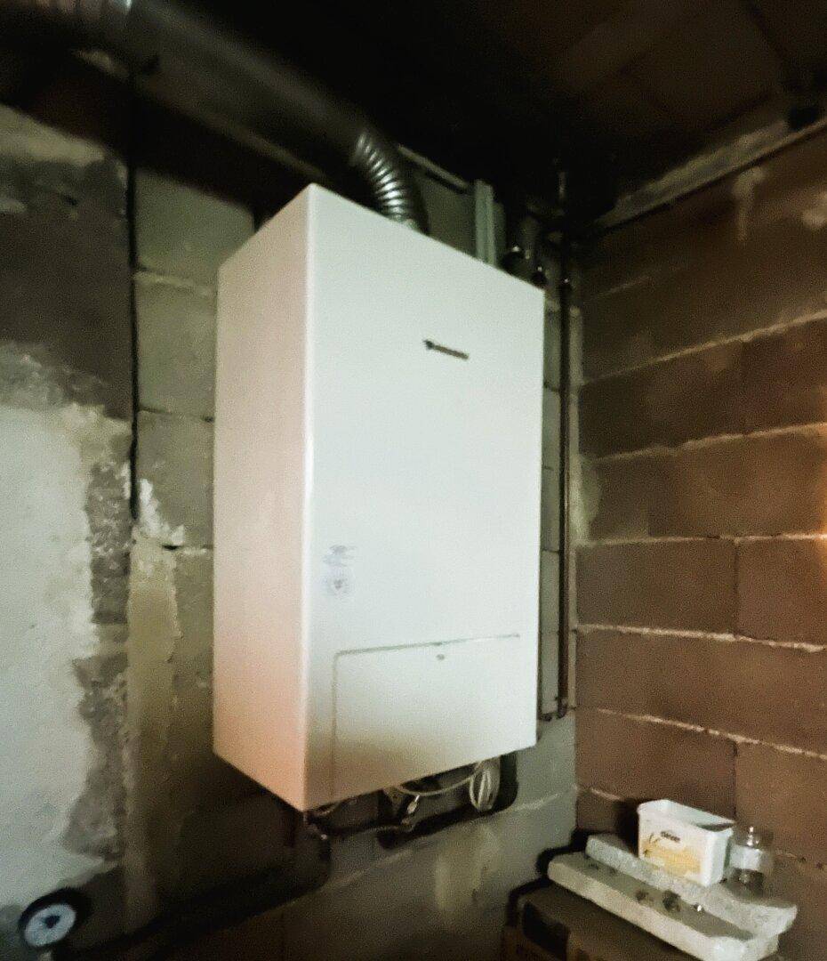 Heizungsraum im Keller mit einem modernen Warmwasserbereiter und unverputzten Wänden.
