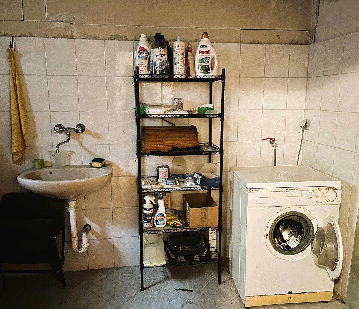 Waschküche im Keller mit Waschmaschine, Waschbecken und Regal für Haushaltsartikel.