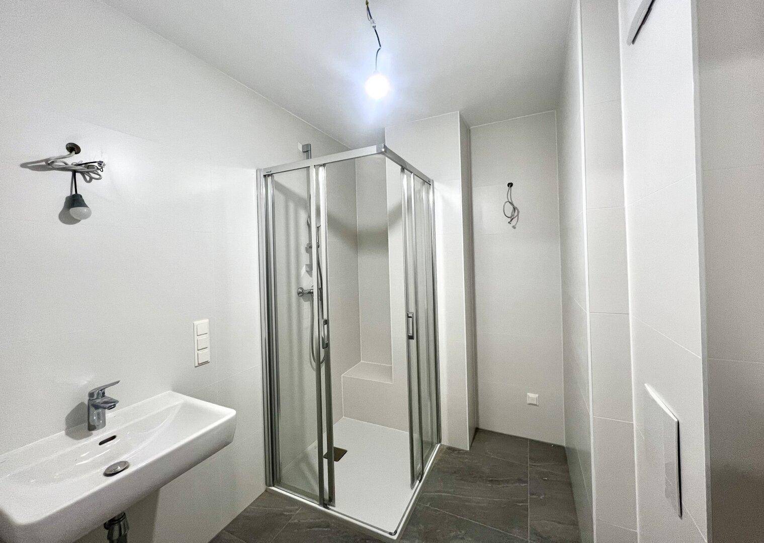 Helles Badezimmer mit Duschkabine, Waschbecken und modernen grauen Fliesen an den Wänden.