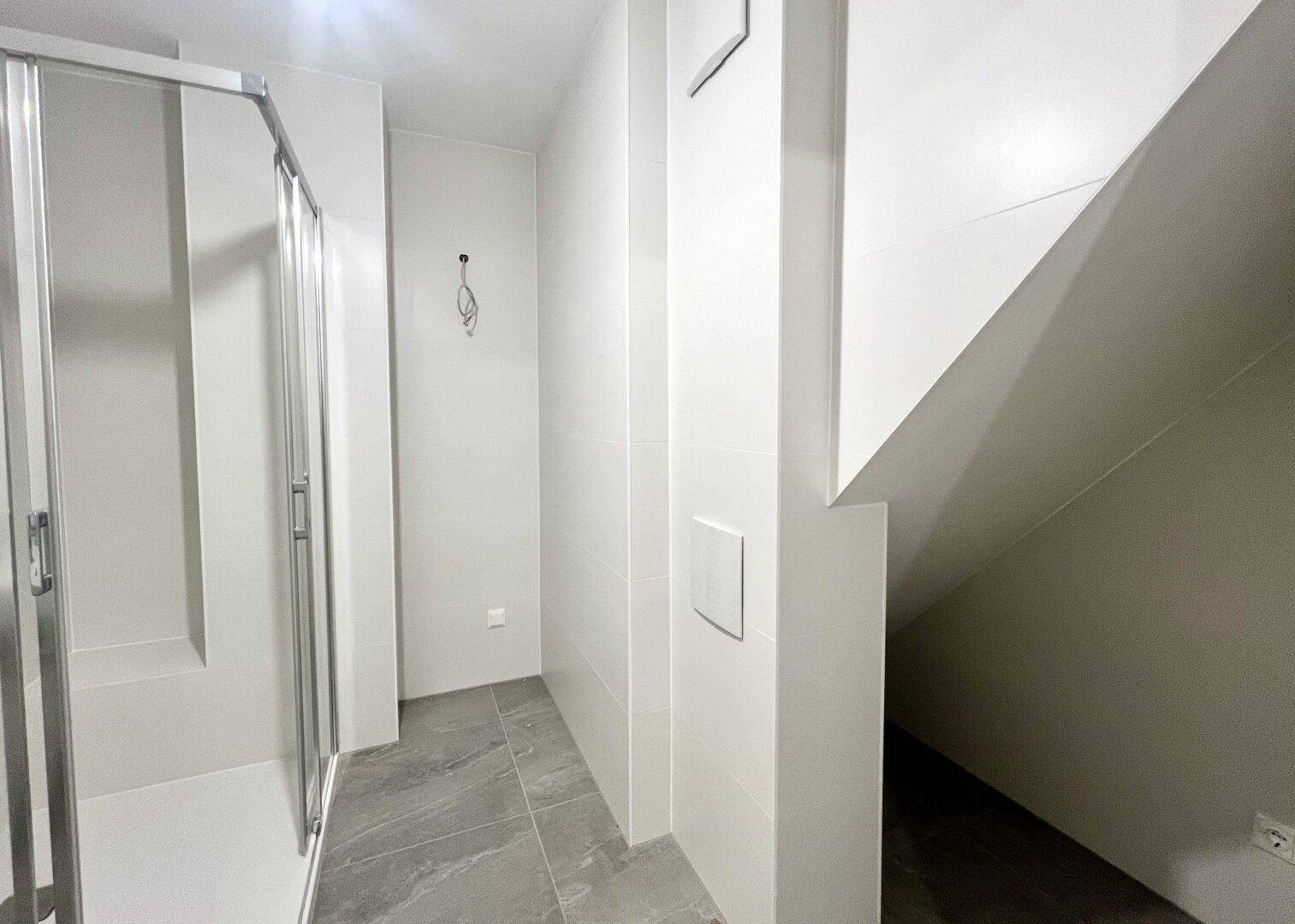 Modernes Badezimmer mit Duschkabine und grauen Fliesen, noch in der Fertigstellungsphase.