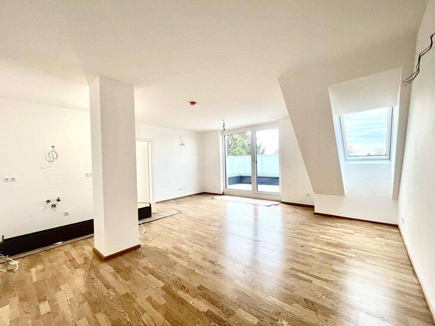 Heller, unmöblierter Raum mit Holzboden, Dachschräge und Zugang zu einer Terrasse.