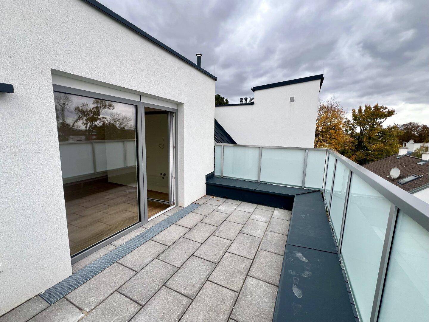 Moderne Dachterrasse mit Steinplattenboden und Glasgeländer, ideal für Entspannung im Freien.