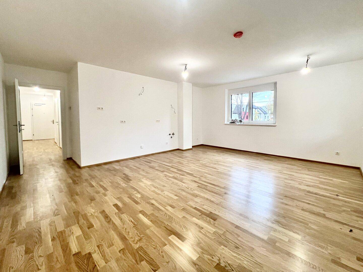 Geräumiger, heller Raum mit Holzparkett und einem Fenster, das den Blick auf die Umgebung freigibt.