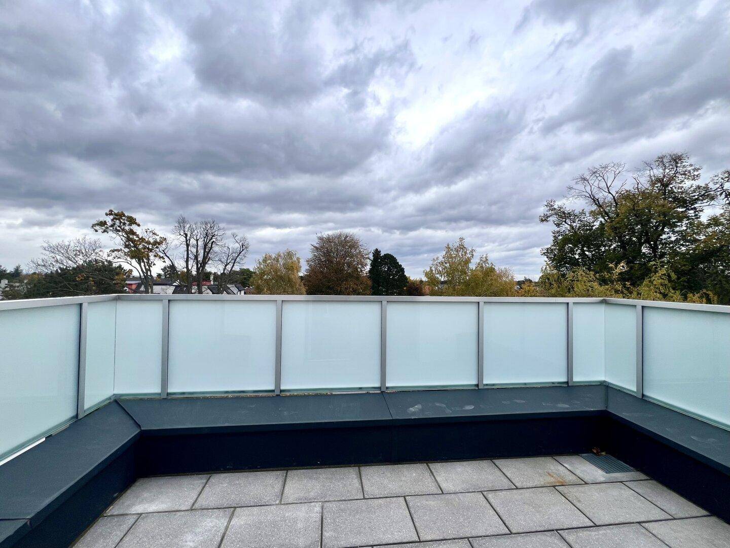 Geräumige Dachterrasse mit moderner Glasbrüstung und weitem Blick ins Grüne unter bewölktem Himmel.