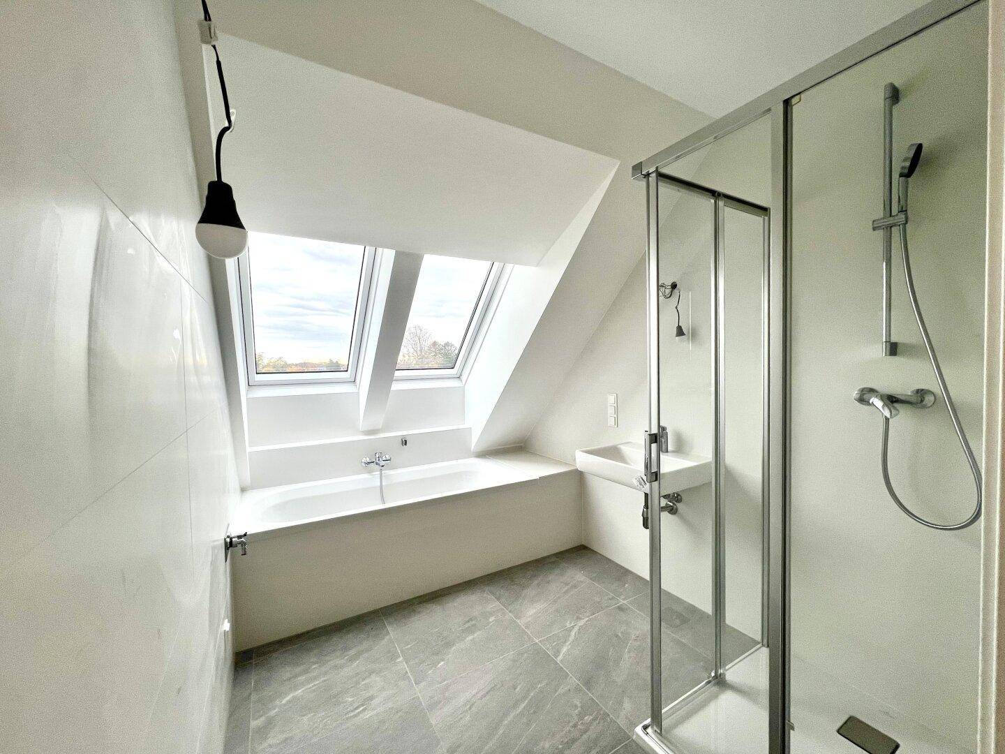 Modernes Badezimmer mit Badewanne, Dusche, grauen Fliesen und Dachfenstern für Helligkeit.