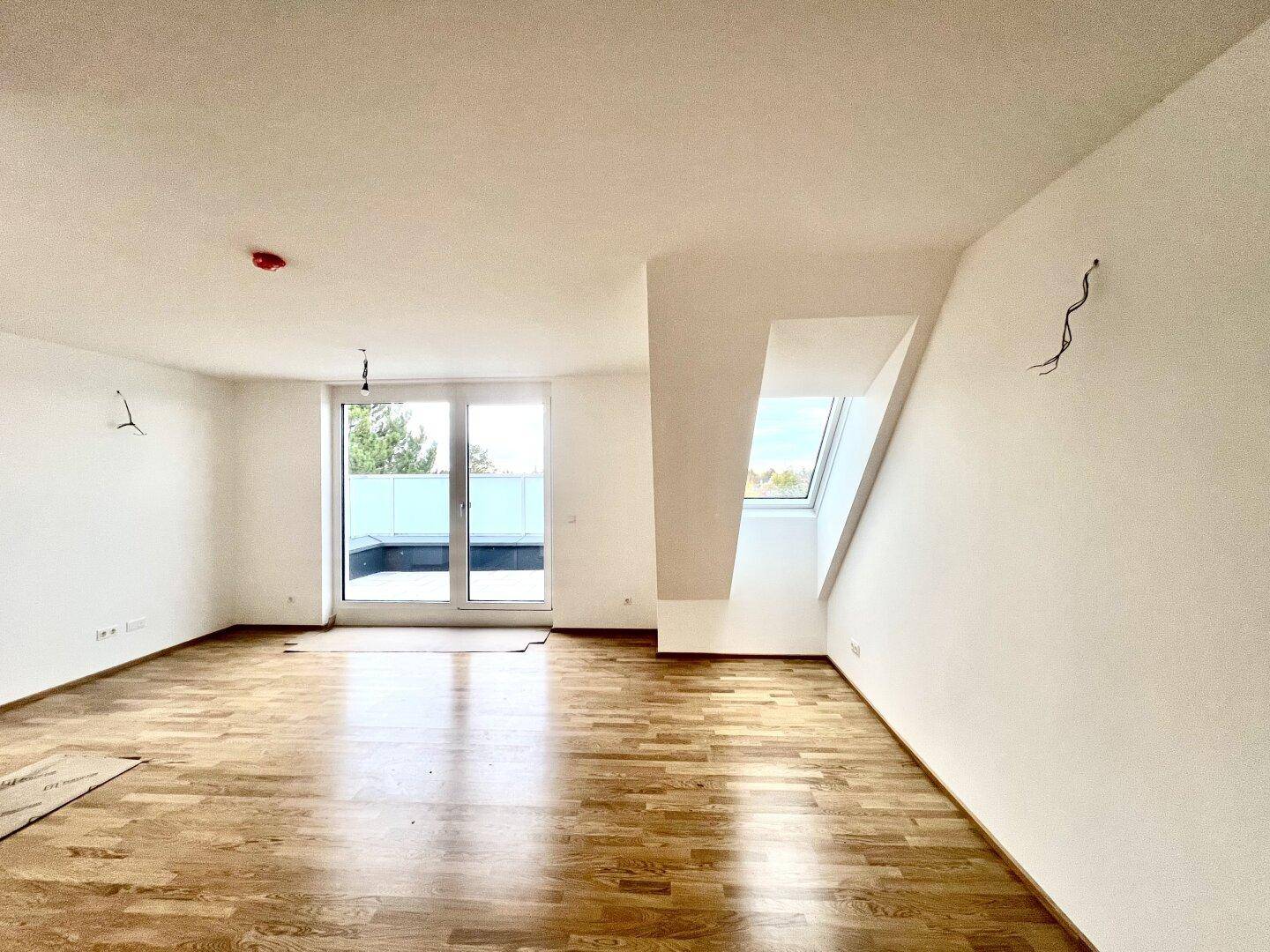 Geräumiges Zimmer mit Holzboden, Dachschräge und breitem Zugang zur Dachterrasse.