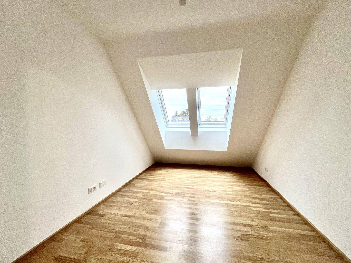 Gemütliches Zimmer mit Holzboden und zwei großen Dachfenstern für viel Tageslicht.