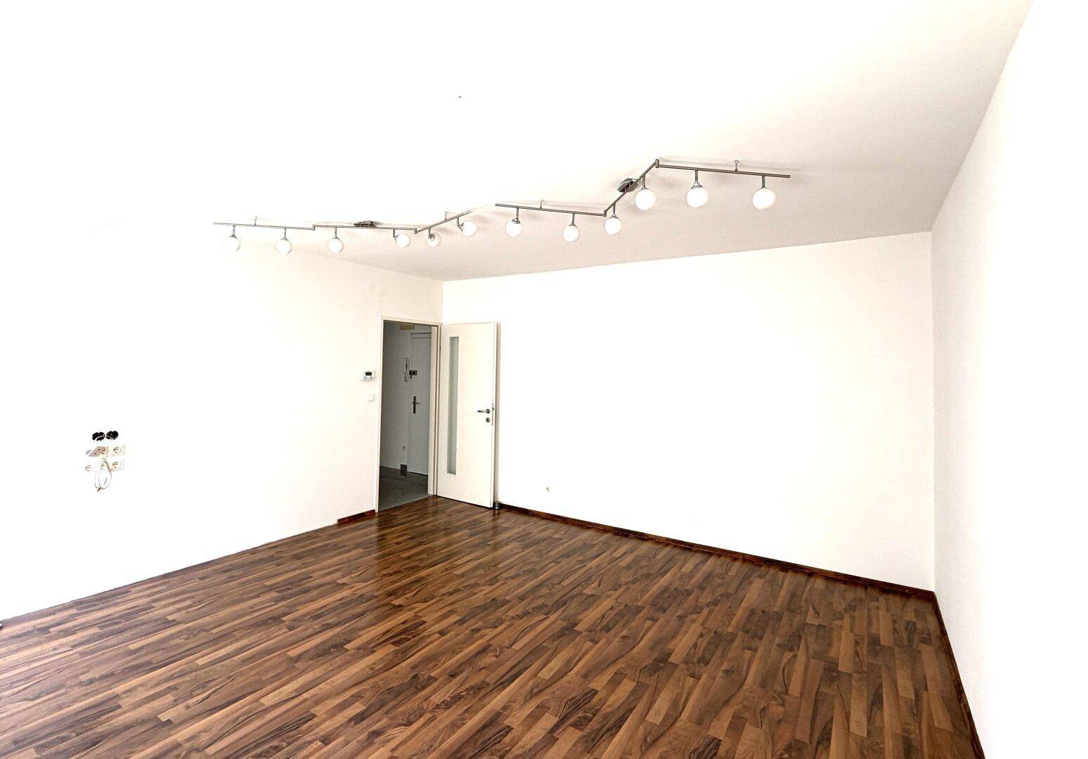 Geräumiges, helles Zimmer mit Holzboden und weiß gestrichenen Wänden, bereit zur Einrichtung.