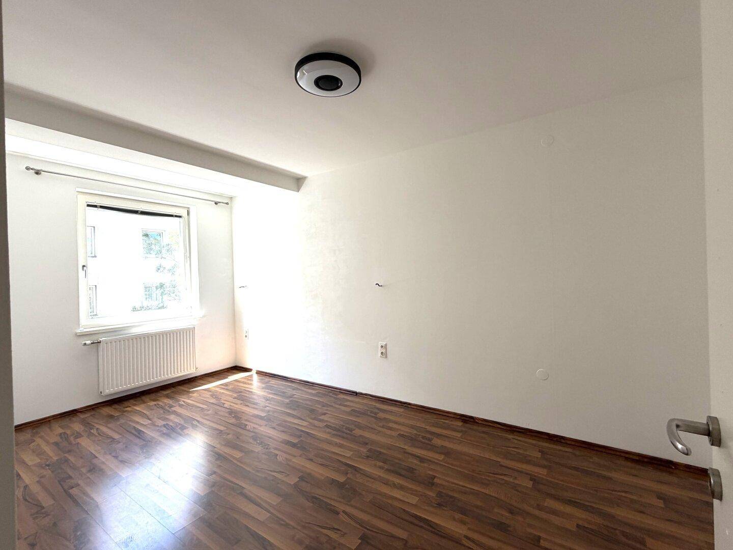 Gemütliches, helles Schlafzimmer mit Holzboden, weiß gestrichenen Wänden und einem Fenster.