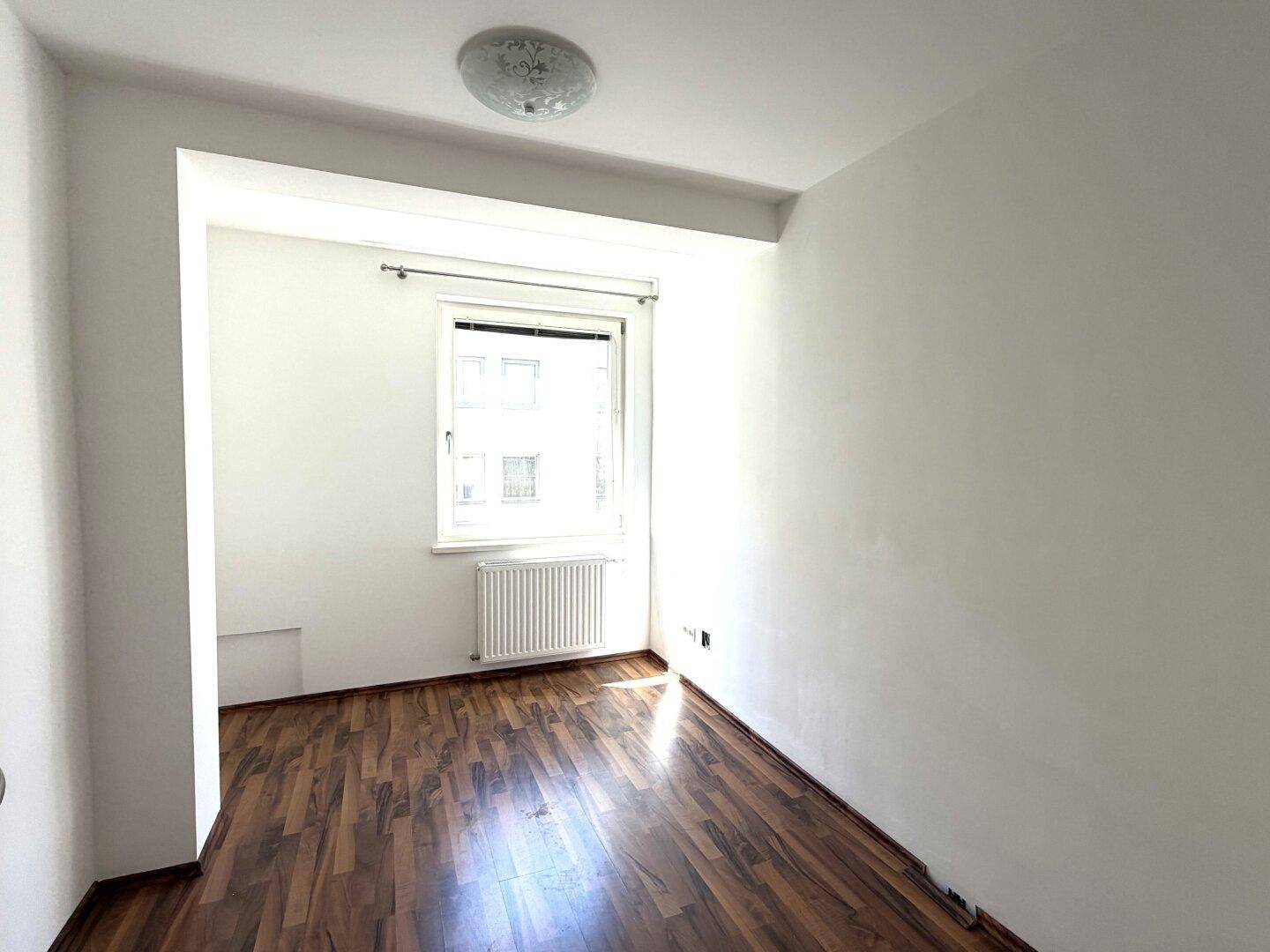 Helles Zimmer mit Holzboden und einem großen Fenster, ideal als Schlaf- oder Arbeitszimmer.