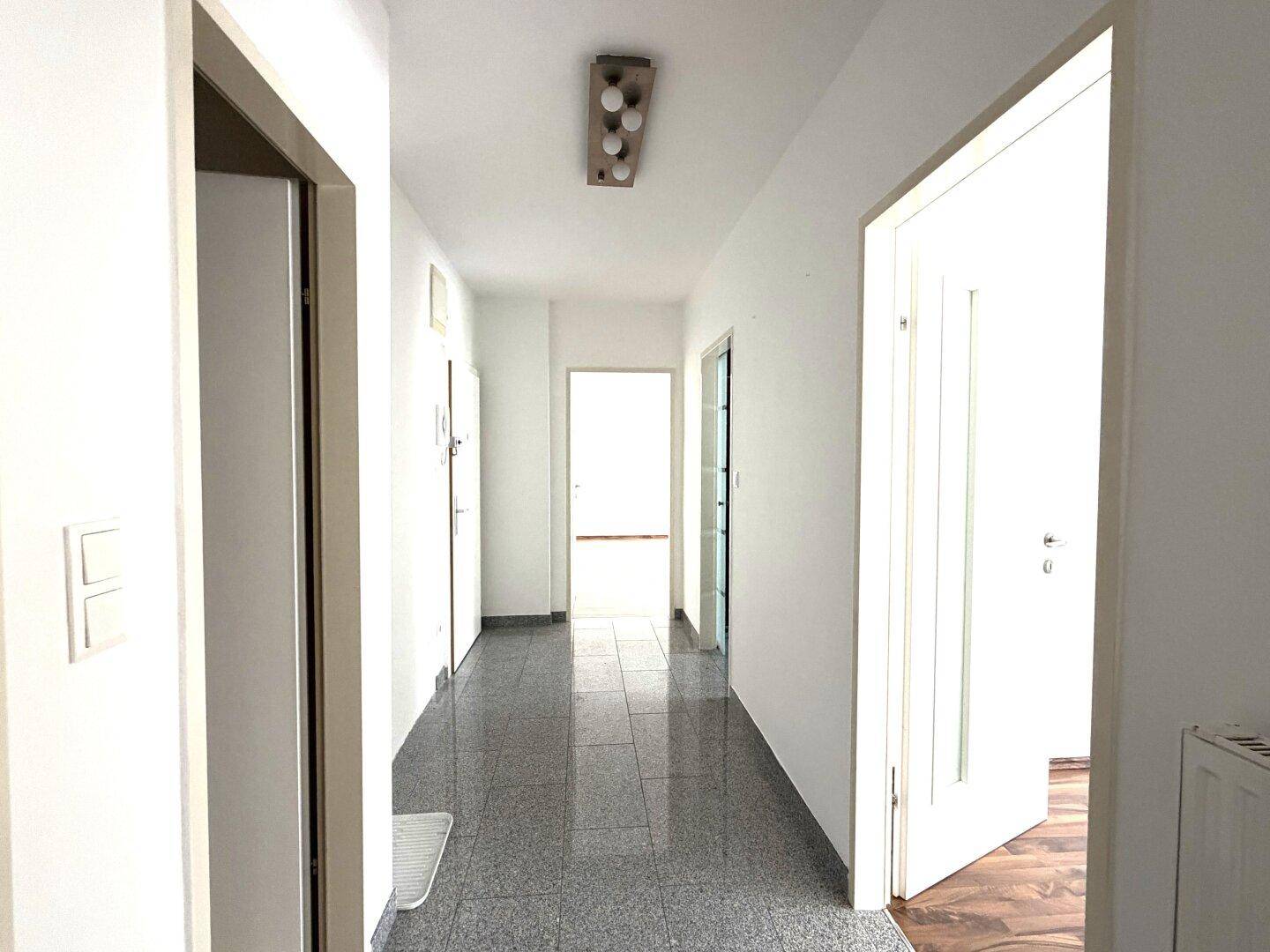 Langer, heller Flur mit Fliesenboden, der zu den verschiedenen Räumen der Wohnung führt.