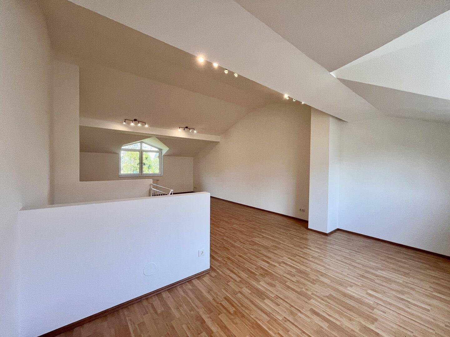 Geräumiger Wohnbereich im Dachgeschoss mit Holzboden, Dachschrägen und Blick ins Grüne.