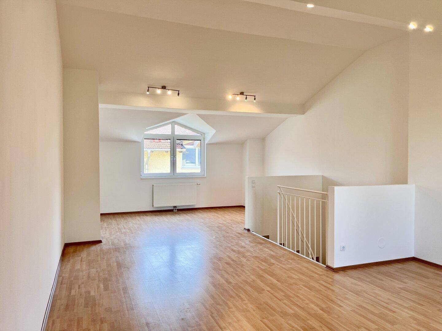 Offener Dachgeschossraum mit Holzboden, Dachschrägen und Blick aus dem Fenster.