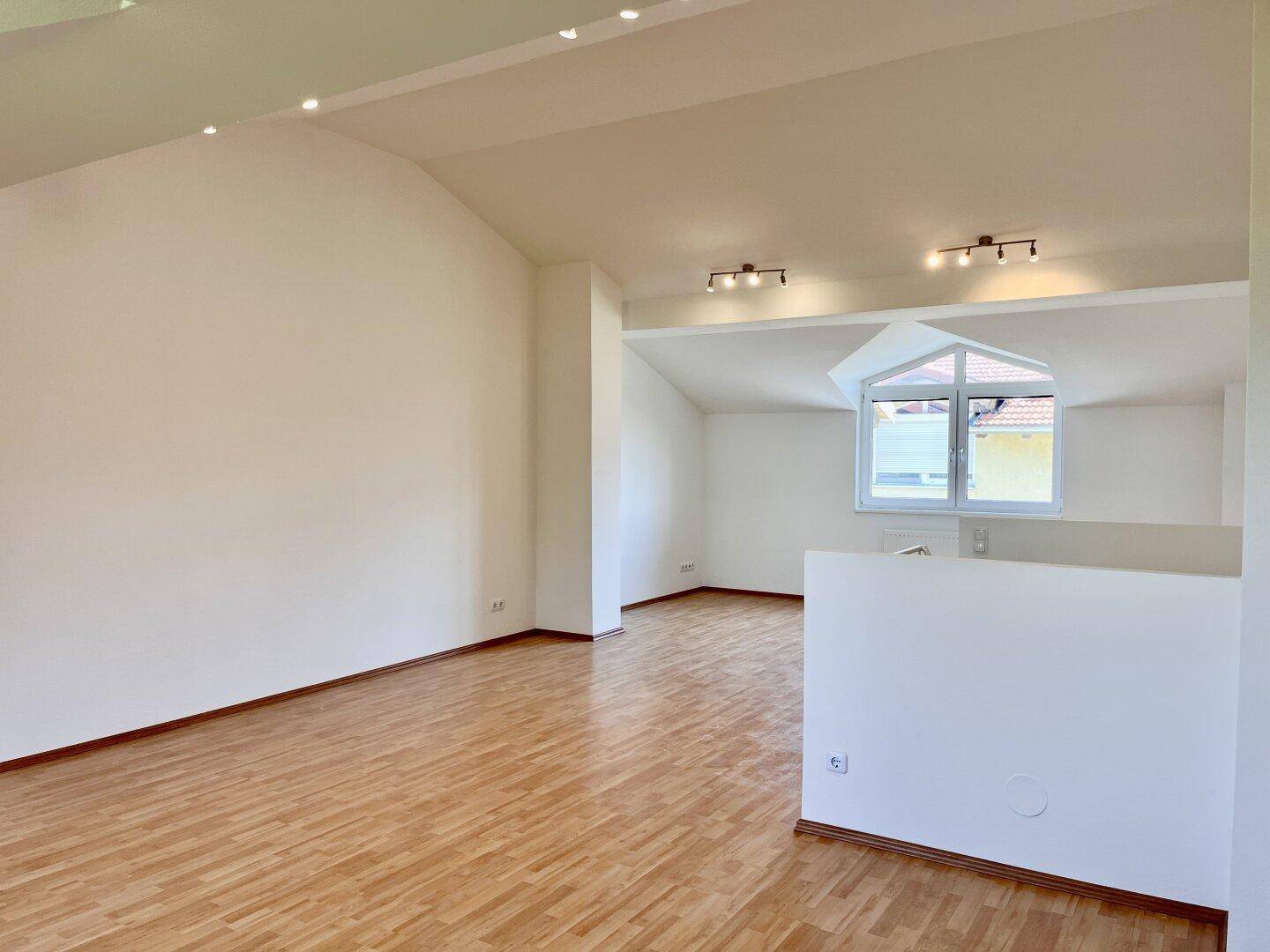 Heller und geräumiger Dachgeschossraum mit Holzboden und schrägen Wänden.