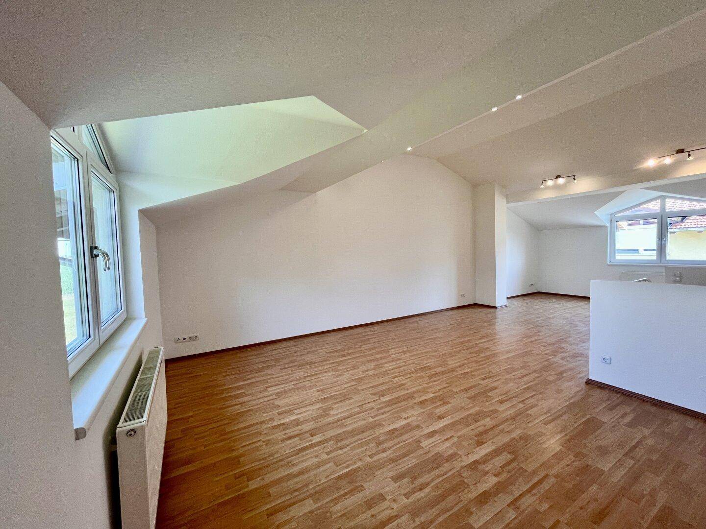 Großer Dachgeschossraum mit Holzboden, viel Tageslicht und Blick nach draußen.