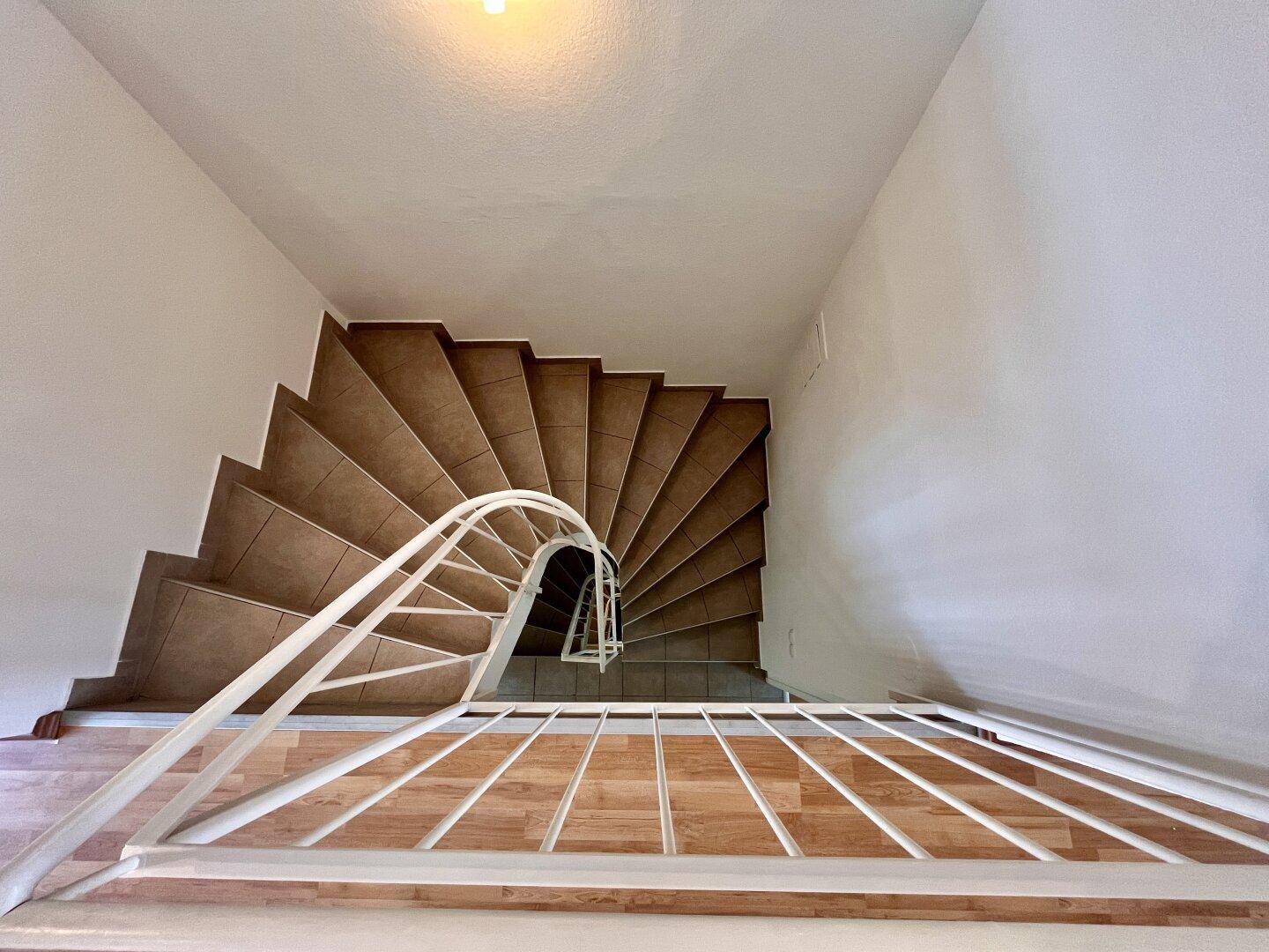 Wendeltreppe mit Fliesenstufen und weißem Geländer, von oben fotografiert.