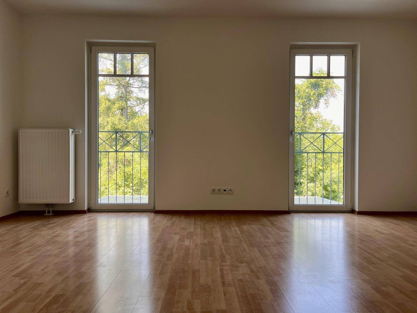 Helles Zimmer mit Holzboden und zwei französischen Balkonen mit Blick ins Grüne.