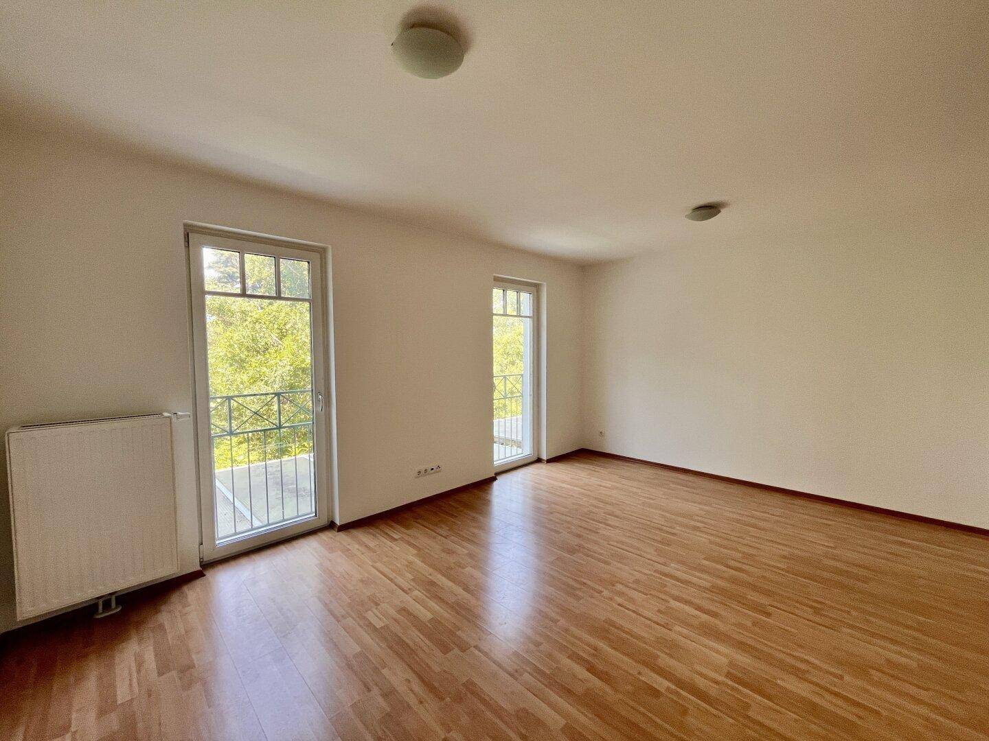 Geräumiges Zimmer mit Holzboden und Zugang zu zwei französischen Balkonen.