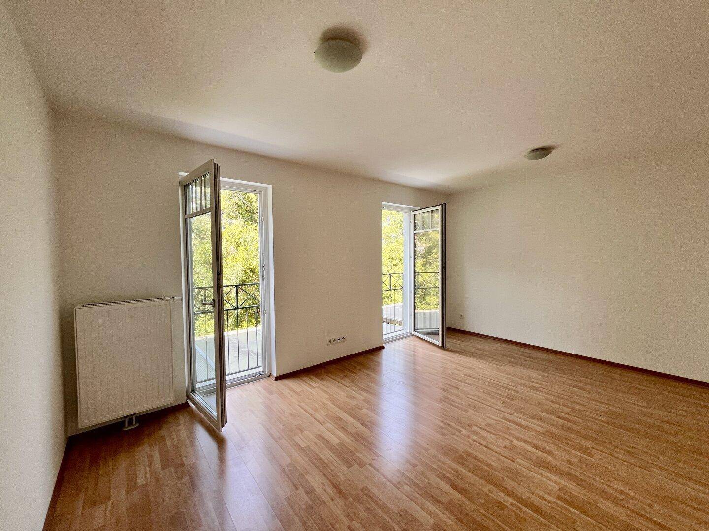 Helles Zimmer mit Holzboden und zwei französischen Balkonen, die viel Licht hereinlassen.