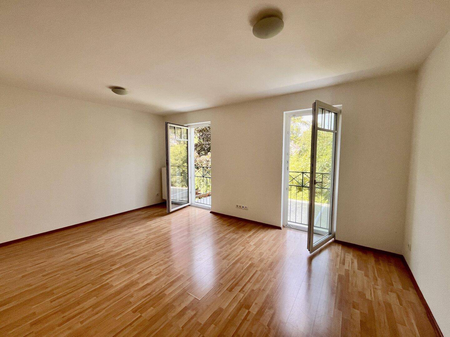 Geräumiges Zimmer mit Holzboden und geöffneten Türen zu den französischen Balkonen.