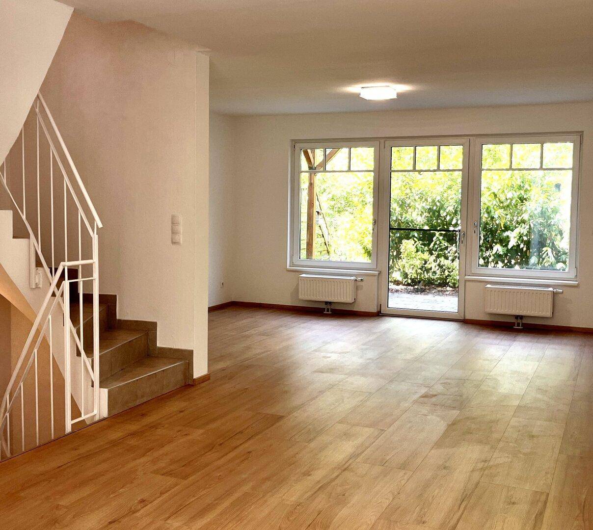 Heller Wohnbereich mit Holzboden und großen Fenstern mit Blick in den Garten.