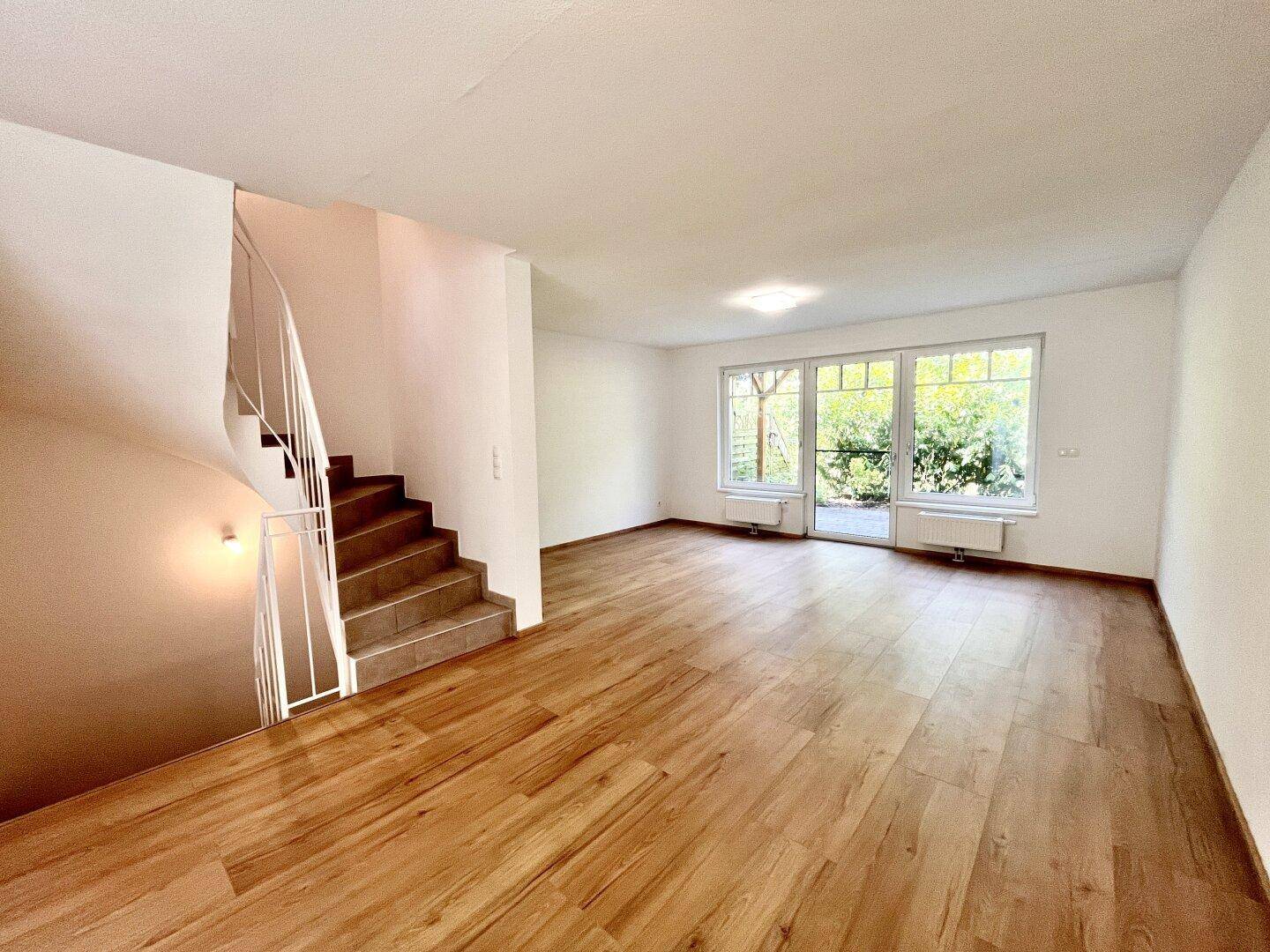 Geräumiger Wohnbereich mit Holzboden, Treppe und großen Fenstern zum Garten.