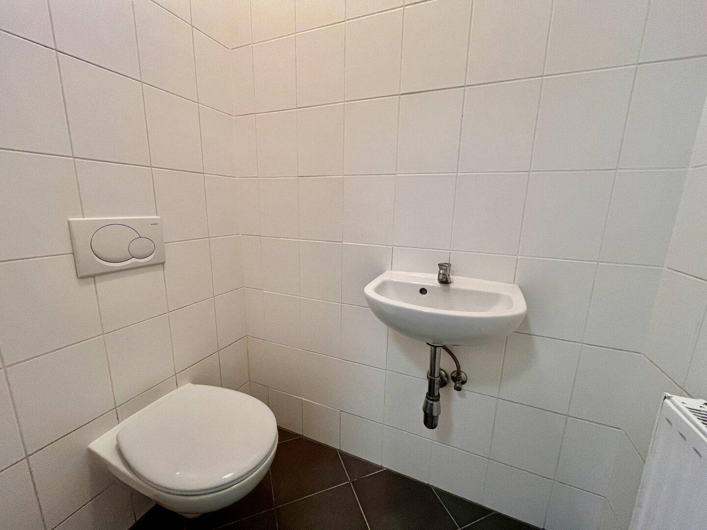 Modernes Gäste-WC mit weißen Wandfliesen, wandhängendem WC und kleinem Waschbecken.
